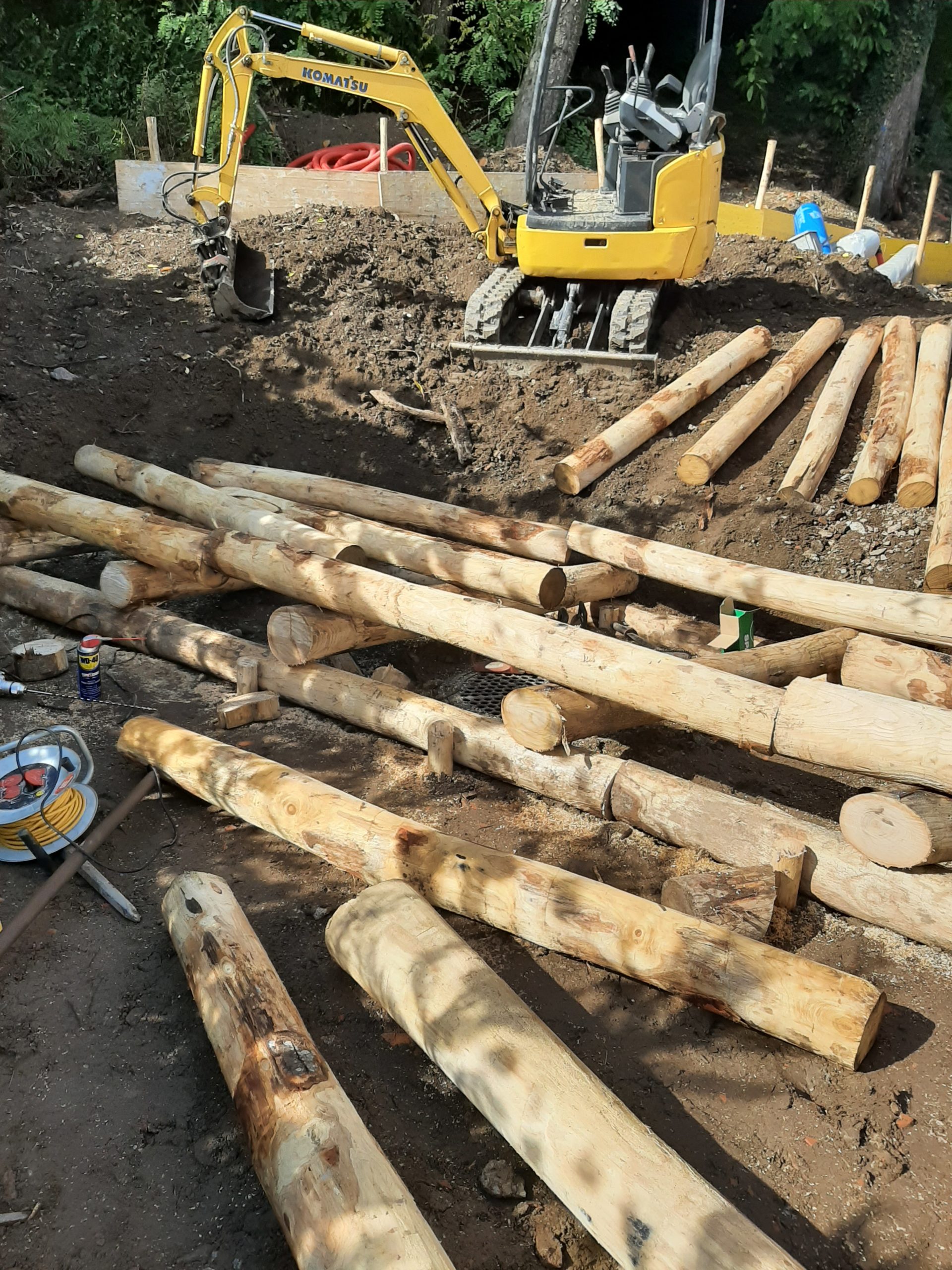 Escavatore giallo in cantiere con tronchi di legno.